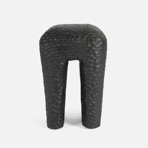 A modern sculptural stool with a textured, hammered finish in dark charcoal gray, shown against a plain light gray background.