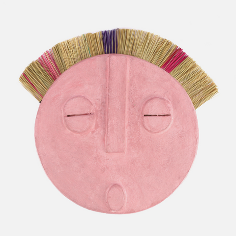 A handmade African mask, predominantly pink in color, with a design that includes geometric shapes and natural elements, displayed against a white background.