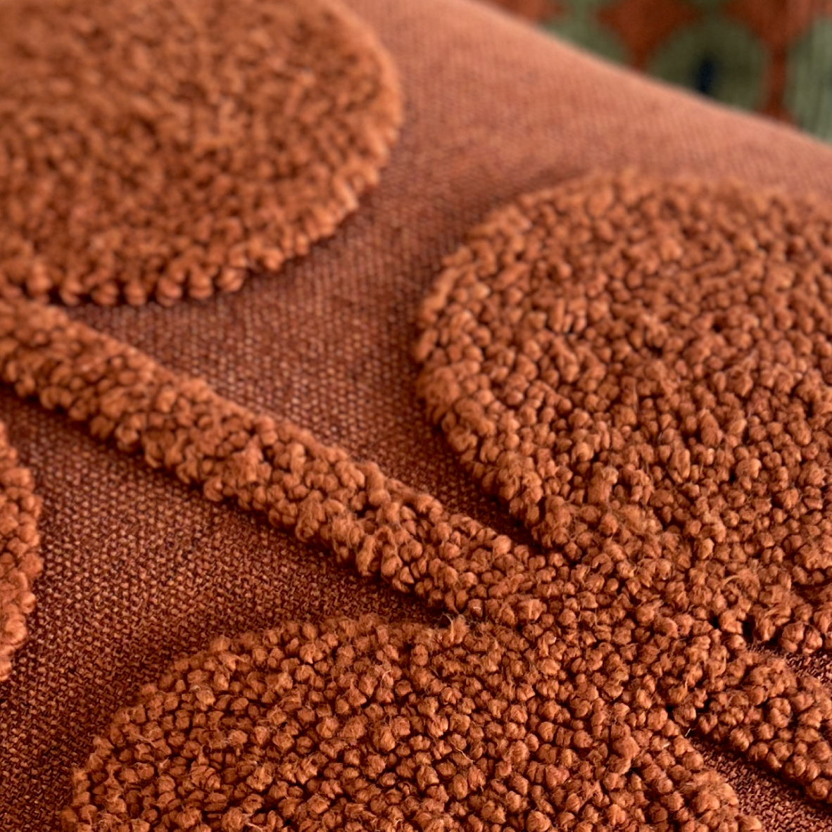 Close-up of a terracotta brown textured throw pillow featuring raised circular and curved tufted patterns on a woven fabric background.