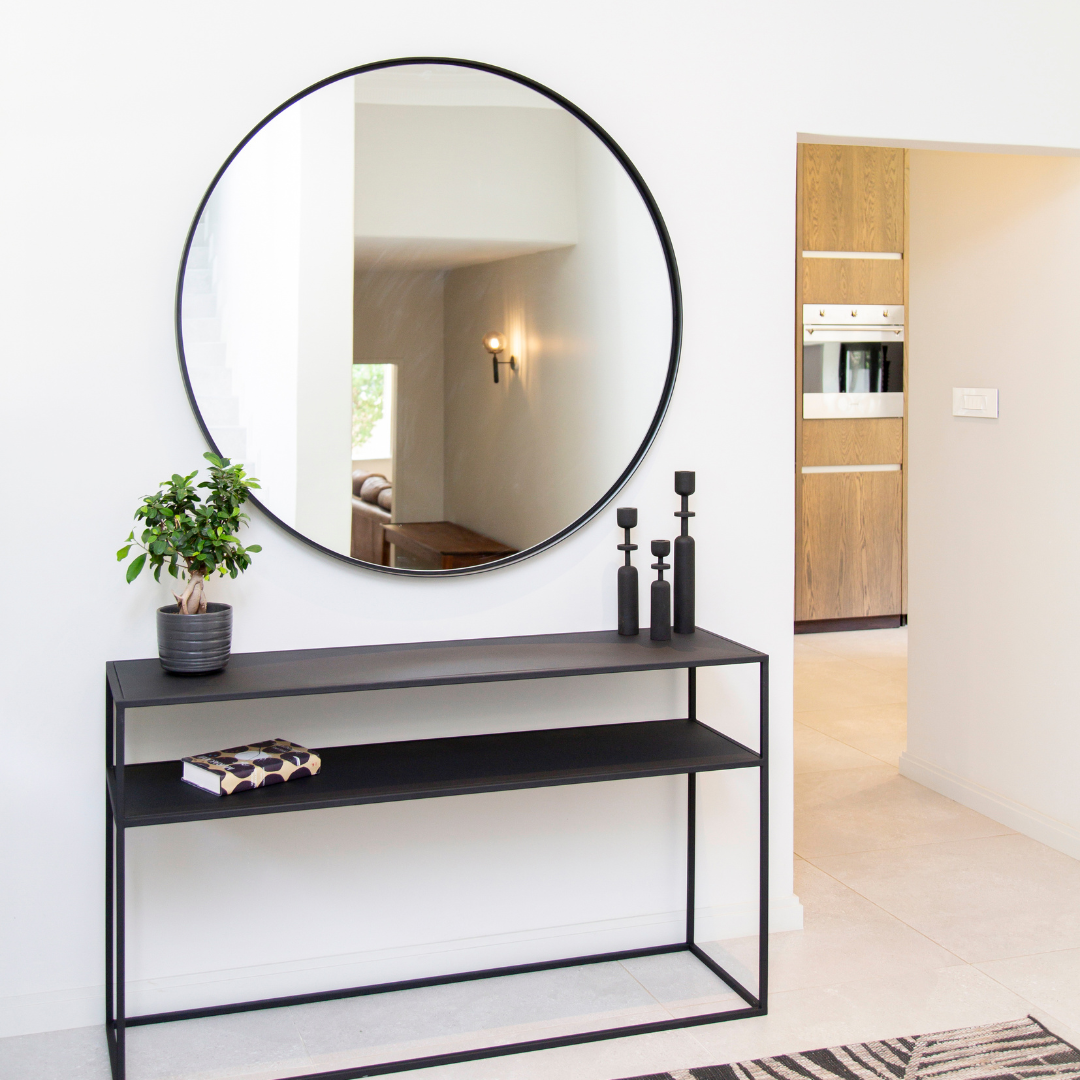 Modern black console table with round mirror and decorative items in a home setting