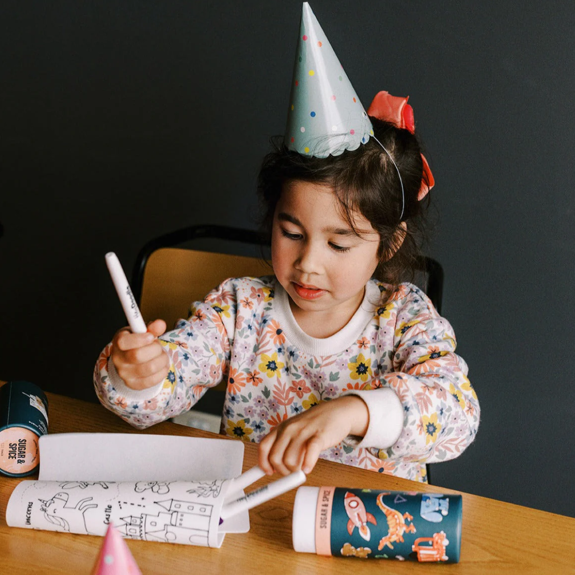 Child wearing a party hat, sitting at a table with coloring books and markers.