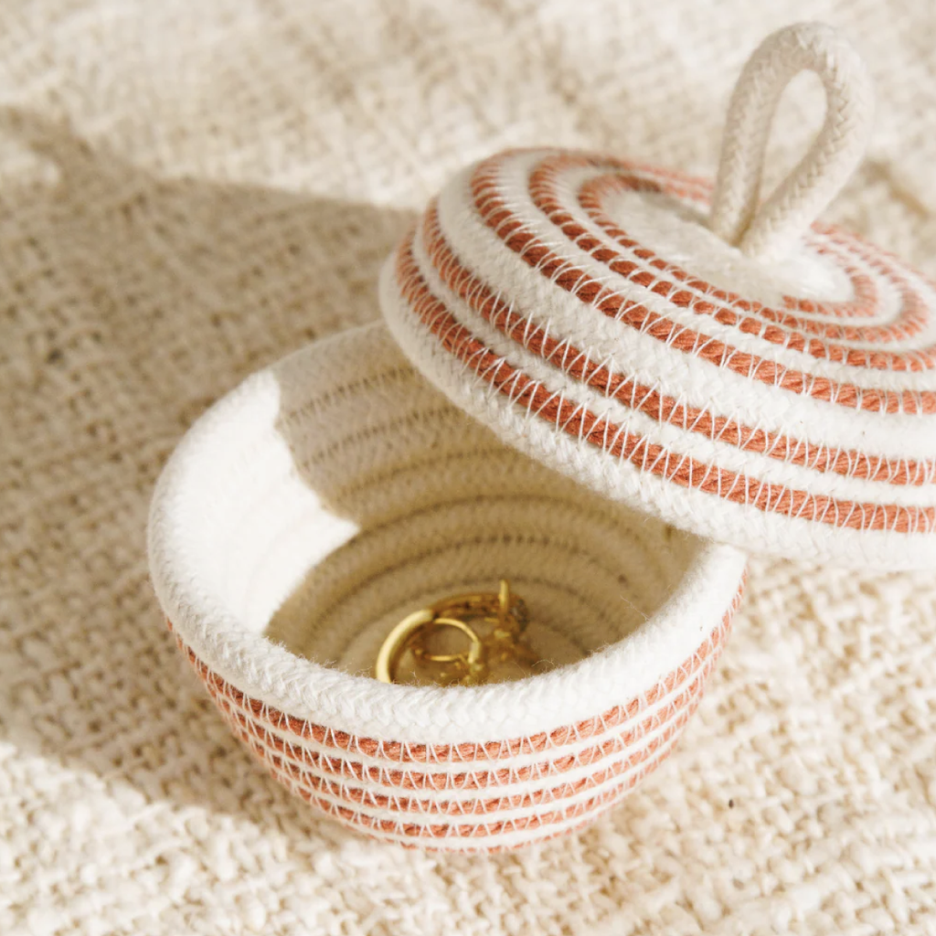 Woven jewelry box with a lid open, revealing a gold ring inside, on a textured beige surface.