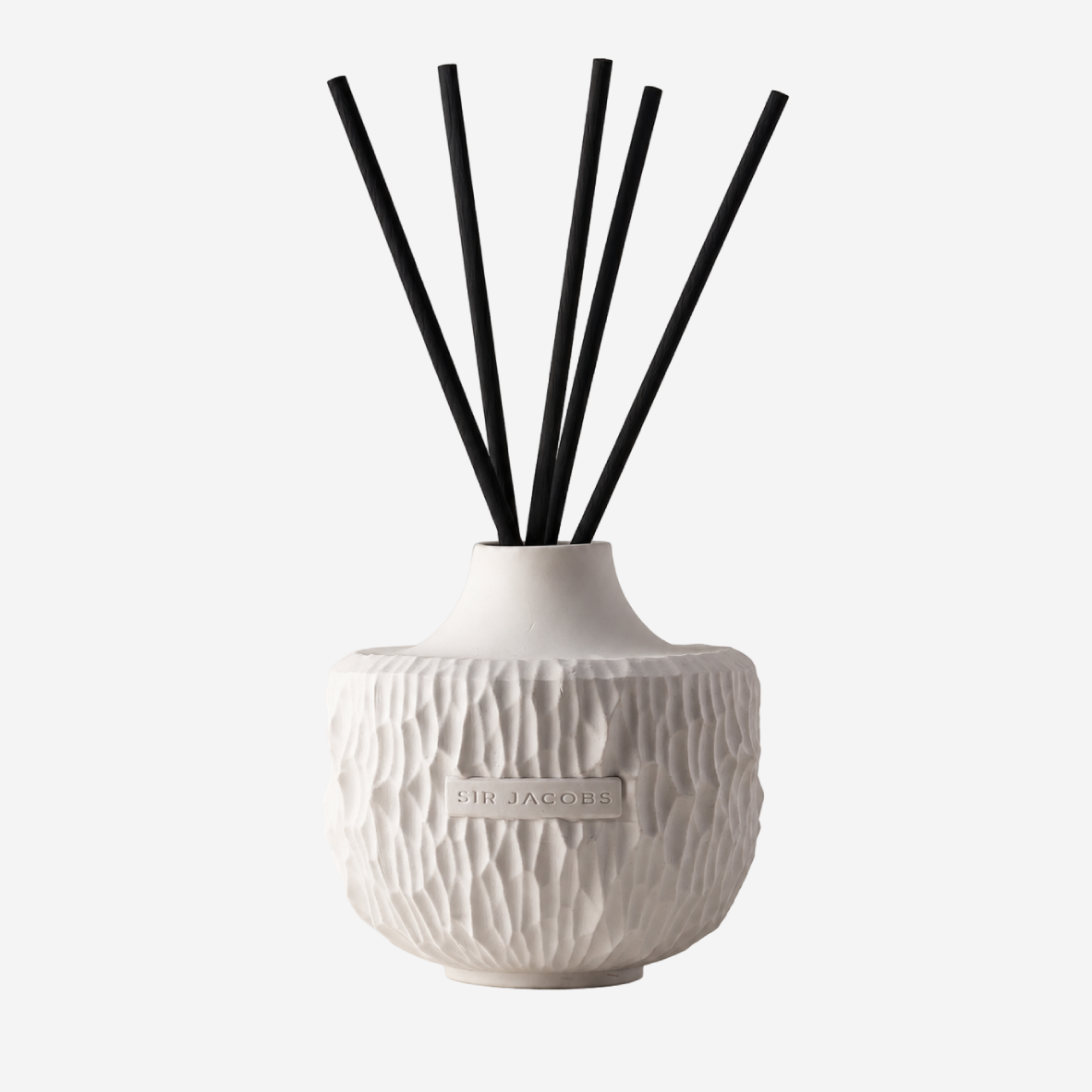 A reed diffuser with a textured white ceramic vase and six black reed sticks, shown against a light gray background.