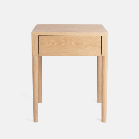 A light natural oak wood side table with a single drawer and four tapered legs, shown against a plain white background.