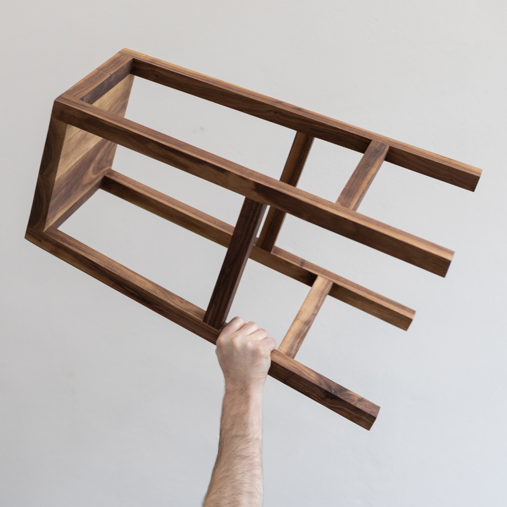 A Japandi style kitchen stool, locally made from solid Walnut being held in the air 