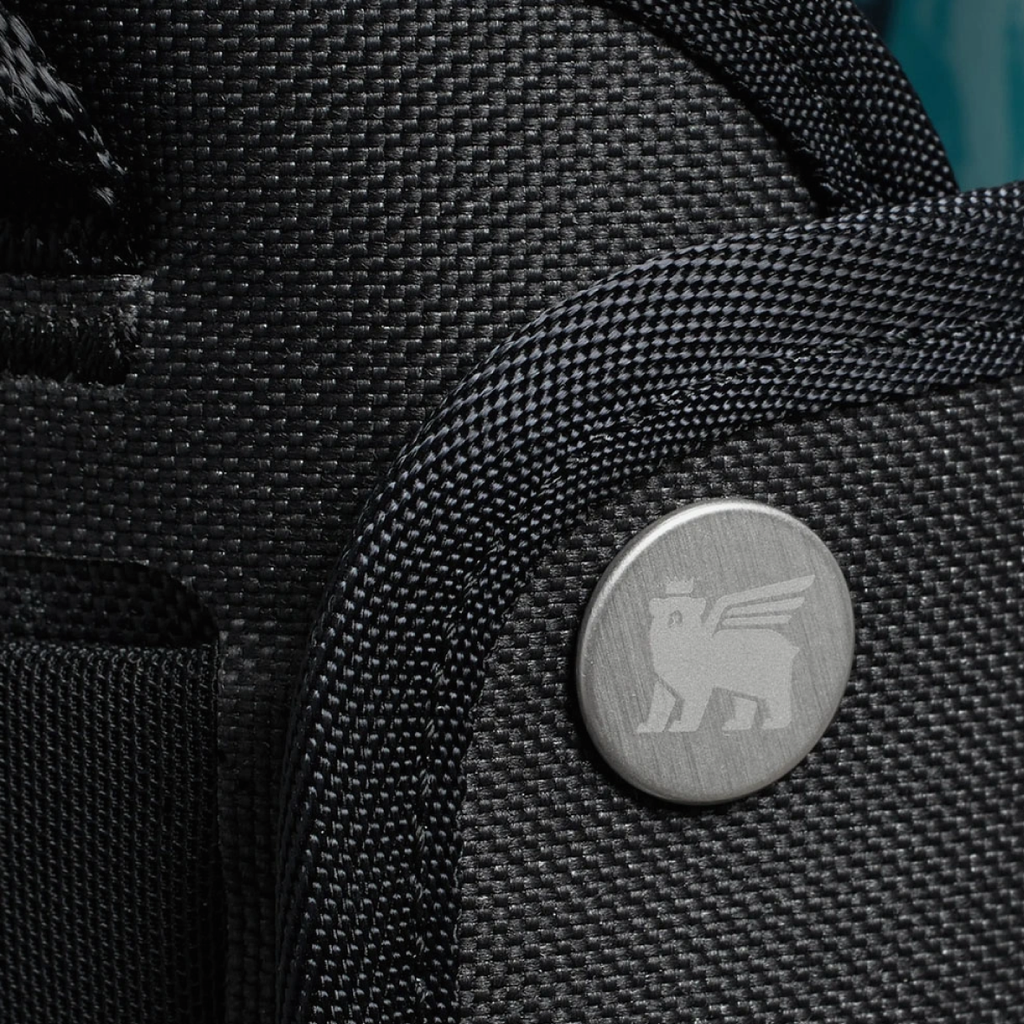 Close-up of a black textured bag with a metallic logo on a blurred background