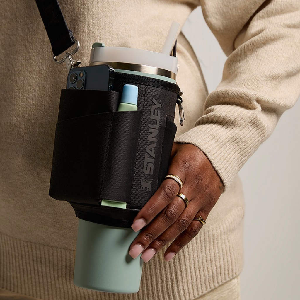 Person holding a Stanley insulated cup holder with a light blue cup inside, wearing a beige sweater.