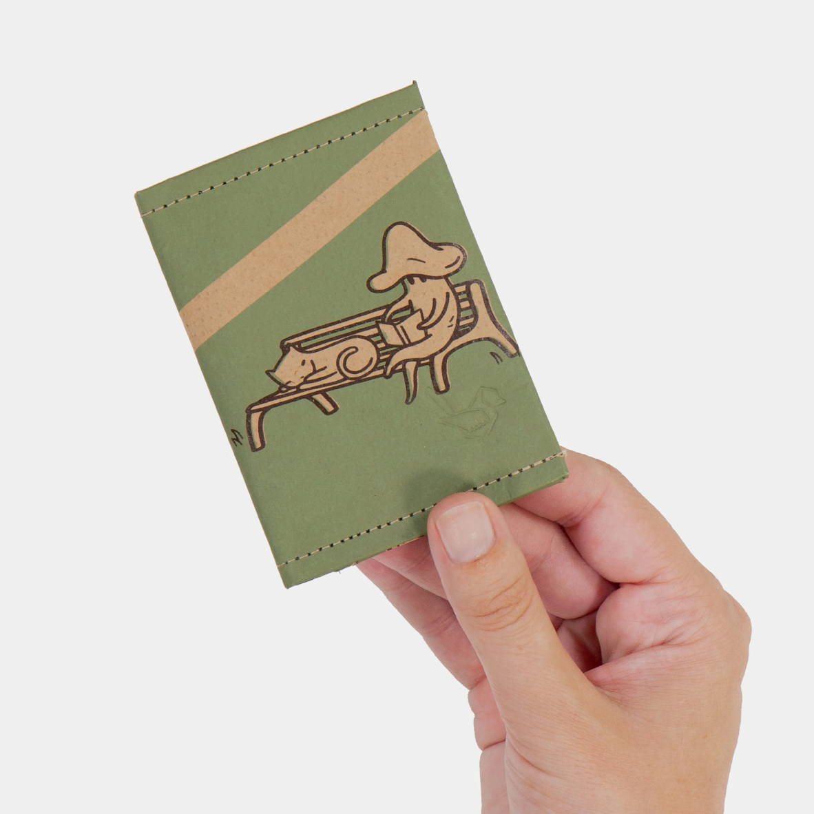 Green cardholder with a brown design of a person sitting on a bench, held by a hand against a white background.